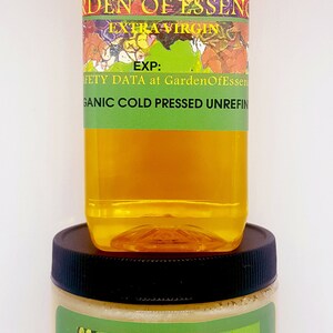 May include: Two bottles of organic cold-pressed jojoba oil and butter from Garden of Essences. The jojoba oil bottle is clear with a yellow liquid and a green label with the text "Jojoba Oil Garden of Essences Extra Virgin EXP: Safety Data at GardenOfEssences Organic Cold Pressed Unrefined". The jojoba butter jar is white with a green label with the text "Jojoba Butter Garden of Essences RAW and UNREFINED GARDENOFESSENCES on etsy.com Read Safety Data at GardenOfEssences.com ORGANIC COLD PRESSED".