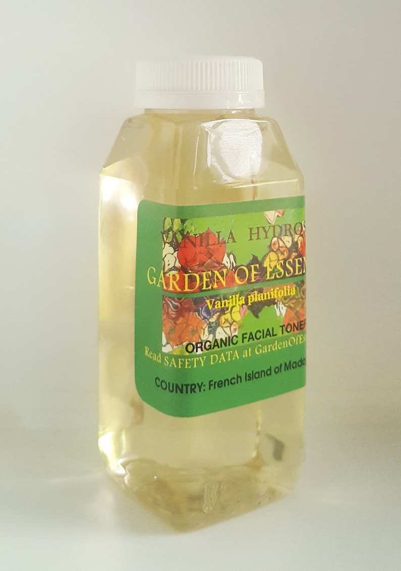 May include: A clear glass bottle with a white cap, containing a yellow liquid. The label is green with white text that reads "Vanilla Hydro Garden of Essen Vanilla planifolia Organic Facial Toner Read Safety Data at GardenOfEss Country: French Island of Made".