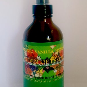 May include: A brown glass bottle with a black spray top and a green label. The label has a colorful floral design and the text "ORGANIC VANILLA HYDRO", "GARDEN OF ESSENCE", "BOTANICAL NAME: Vanilla plant", "COUNTRY: French Island of Madagascar", and "SAFETY DATA at GardenOfEssence".