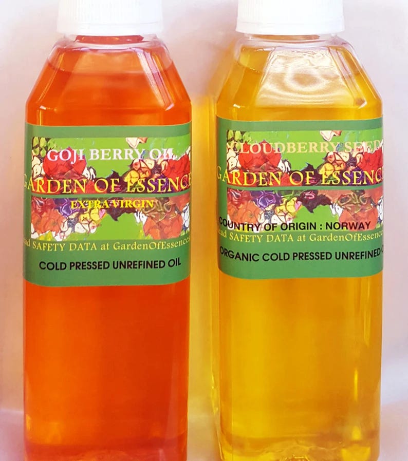 Puede incluir: Dos botellas de pl&aacute;stico transparente llenas de aceite naranja y amarillo. Las botellas tienen tapas blancas y etiquetas verdes con dise&ntilde;os florales y texto que dice "GOJI BERRY OIL" y "LOUDBERRY SEED". Las etiquetas tambi&eacute;n indican "COLD PRESSED UNREFINED OIL".