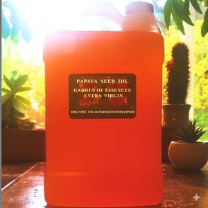 K&ouml;nnte beinhalten: Ein gro&szlig;er, durchscheinender orangefarbener Kunststoffkanister mit Fl&uuml;ssigkeit und einem schwarzen rechteckigen Etikett, das die Aufschrift PAPAYA SEED OIL, GARDEN OF ESSENCES, EXTRA VIRGIN und ORGANIC COLD PRESSED UNREFINED in Gold tr&auml;gt.