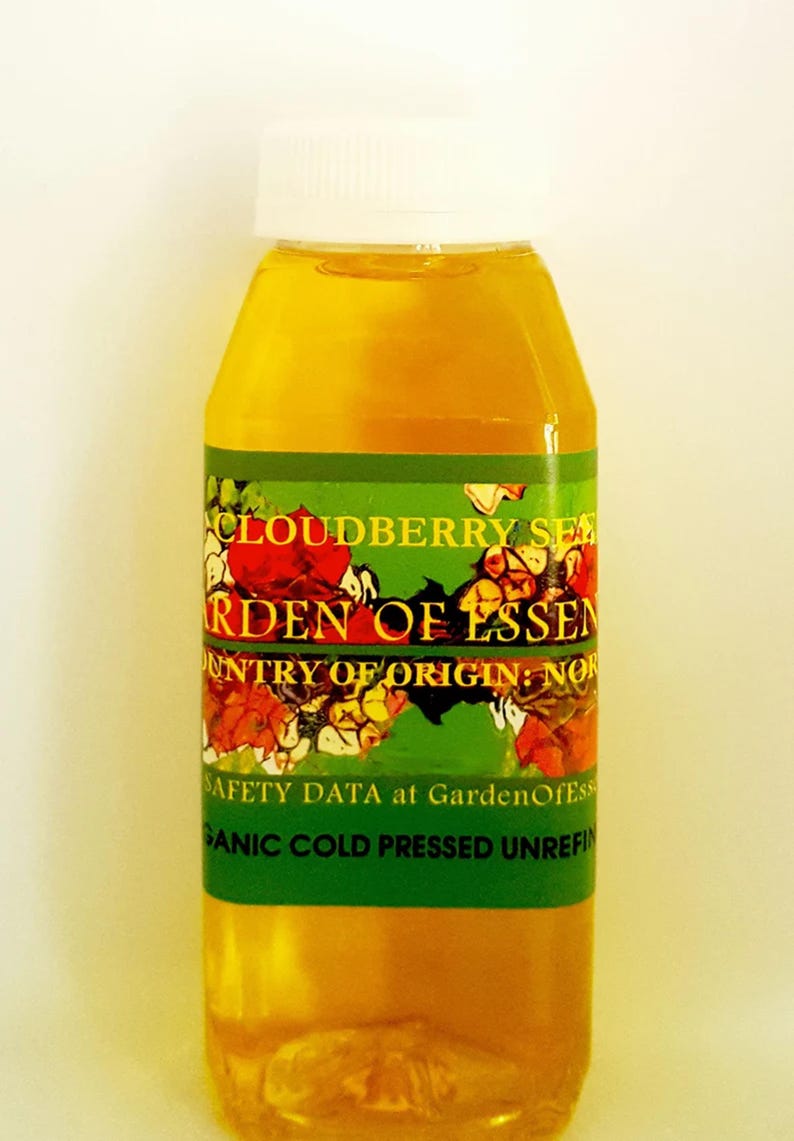 Puede incluir: Botella transparente llena de l&iacute;quido dorado, con tapa blanca. La etiqueta verde muestra "CLOUDBERRY SEE" y "GARDEN OF ESSEN", con informaci&oacute;n sobre el origen y el procesamiento. La etiqueta tiene dise&ntilde;os florales.