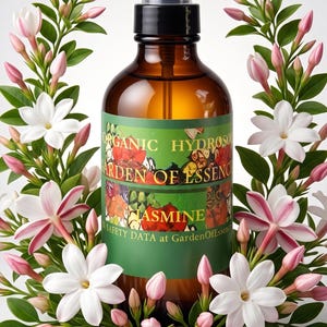 Könnte beinhalten: Eine bernsteinfarbene Glassprühflasche mit einem grünen Etikett mit der Aufschrift ORGANIC HYDROSOL GARDEN OF ESSENCE JASMINE und SAFETY DATA at GardenOfEssence, umgeben von einem Kranz aus weißen Jasminblüten, rosa Knospen und grünen Blättern.