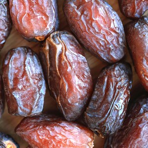 May include: A close-up of a group of dried dates. The dates are a deep brown colour and have a wrinkled texture. They are arranged in a random pattern.