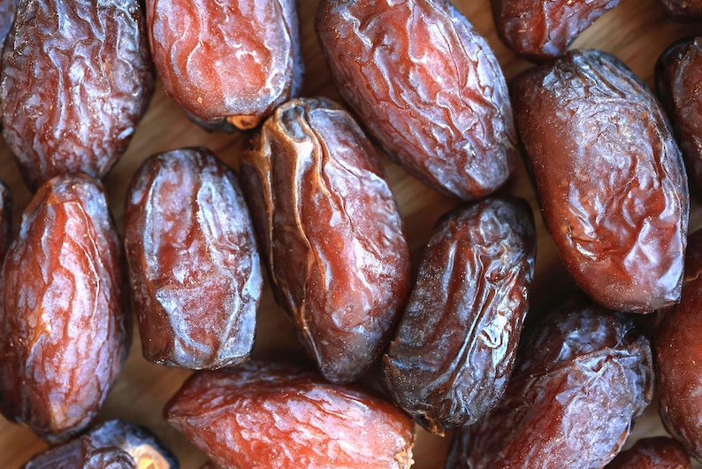 May include: A close-up of a group of dried dates. The dates are a deep brown colour and have a wrinkled texture. They are arranged in a random pattern.