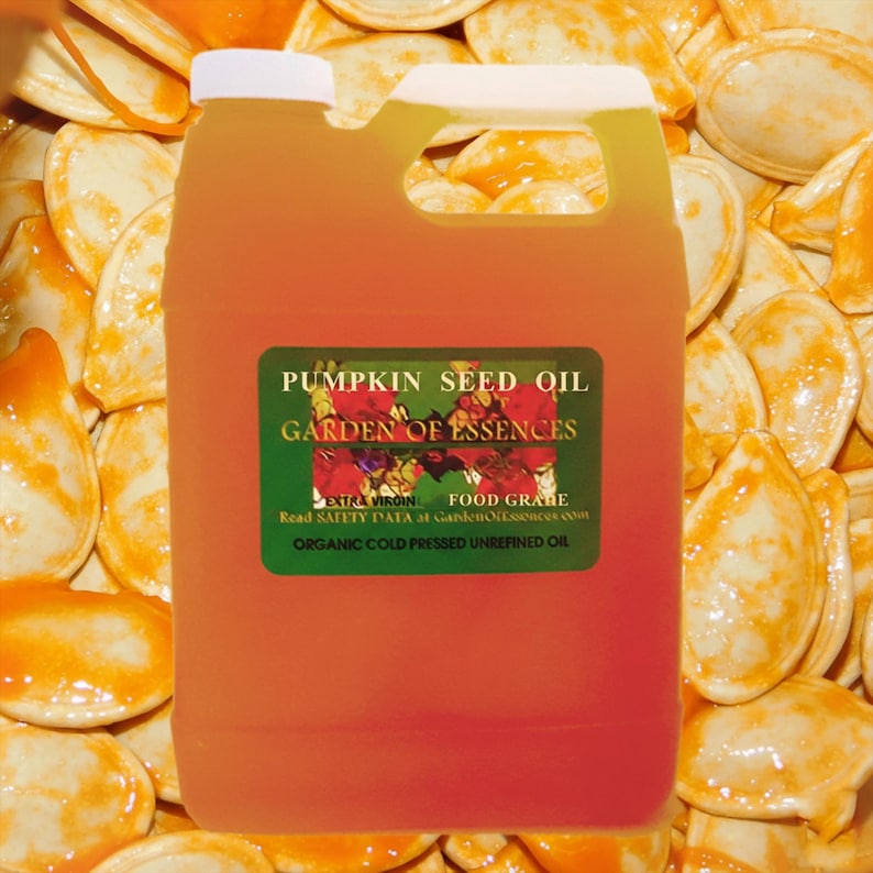 May include: A clear plastic jug filled with orange pumpkin seed oil. The label reads "PUMPKIN SEED OIL GARDEN OF ESSENCES" and includes the text "EXTRA VIRGIN FOOD GRABE ORGANIC COLD PRESSED UNREFINED OIL". The background is filled with pumpkin seeds.