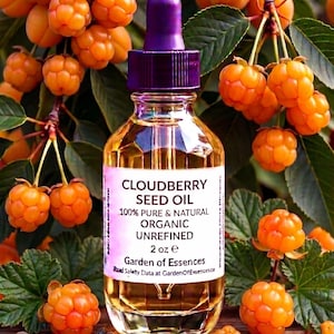 May include: A clear glass bottle of cloudberry seed oil with a purple dropper. The label reads "Cloudberry Seed Oil 100% Pure & Natural Organic Unrefined 2 oz e". The bottle is surrounded by orange cloudberries and green leaves.