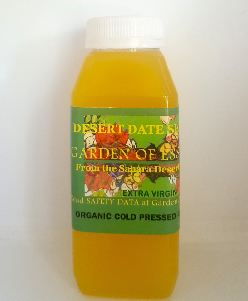 May include: A clear glass bottle with a white cap filled with a yellow liquid. The label reads "Desert Date Seed Oil, Garden of Ess, From the Sahara Desert, Extra Virgin, Organic Cold Pressed".