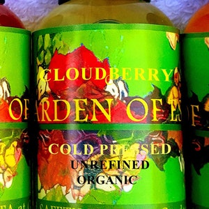 Puede incluir: Botellas de aceite de semillas Cloudberry Garden of Eden. Las etiquetas son verdes con dise&ntilde;os florales coloridos y el texto "Cloudberry", "Cold Pressed", "Unrefined" y "Organic". Las botellas tienen tapas negras.