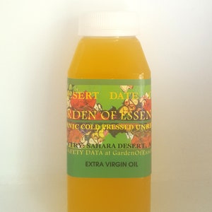May include: A clear glass bottle with a green label that reads "Desert Date Garden of Essen, Organic Cold Pressed Unrefined Extra Virgin Oil". The bottle is filled with a yellow liquid.