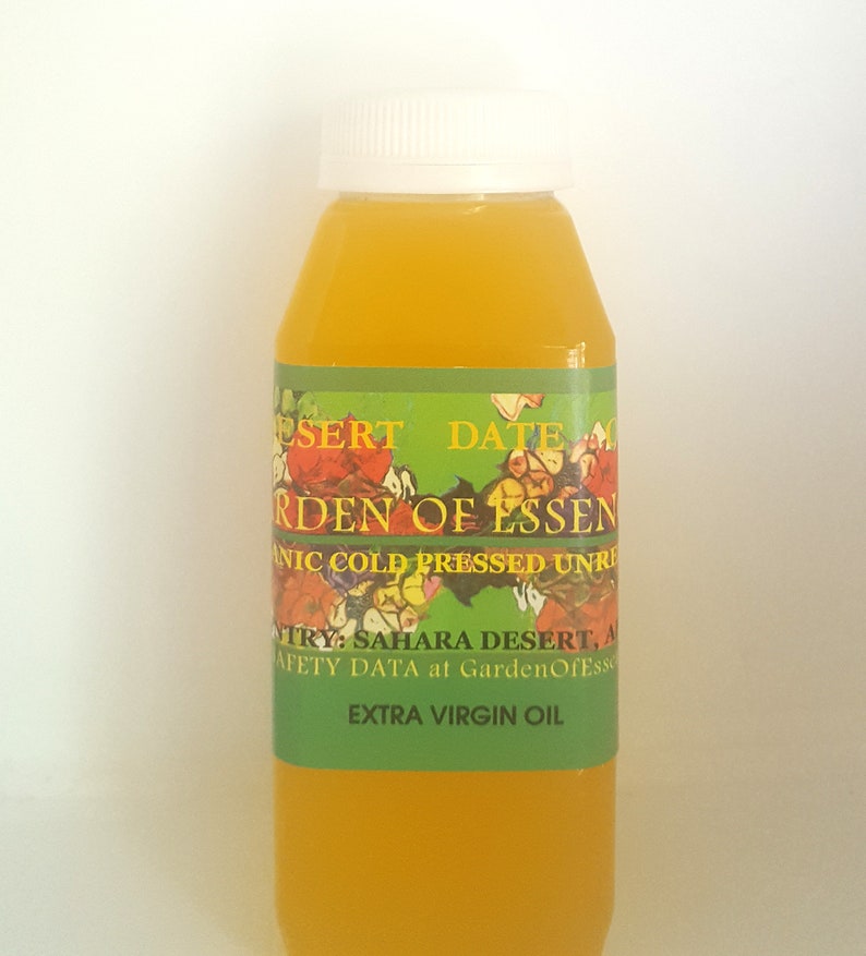May include: A clear glass bottle with a green label that reads "Desert Date Garden of Essen, Organic Cold Pressed Unrefined Extra Virgin Oil". The bottle is filled with a yellow liquid.