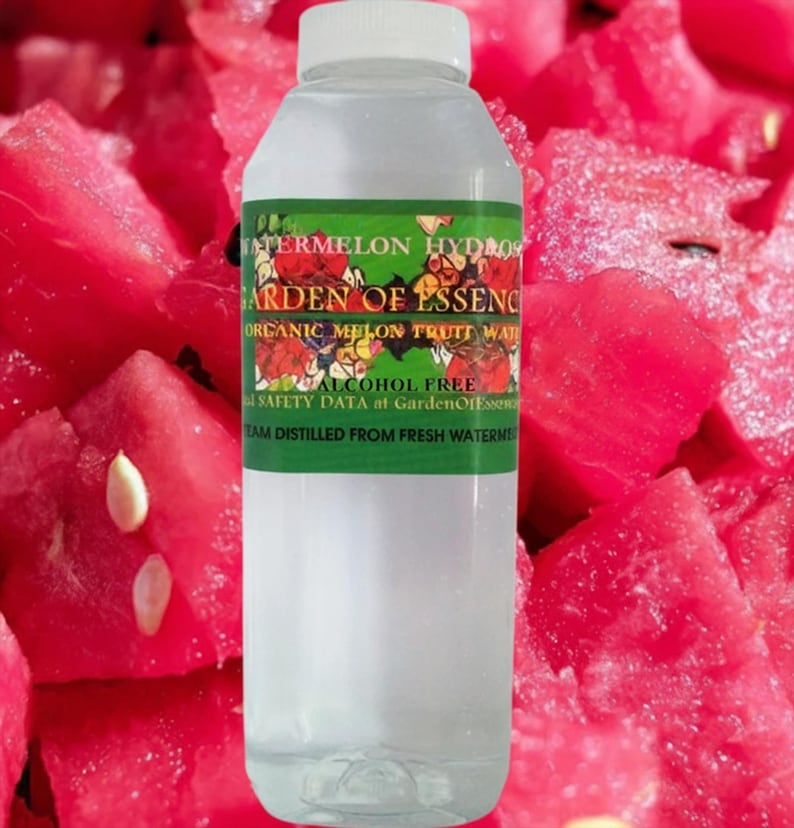 May include: A clear plastic bottle with a white cap, filled with a transparent liquid. The label reads "WATERMELON HYDROS GARDEN OF ESSENCE ORGANIC MELON FRUIT WATER ALCOHOL FREE". The background features bright red watermelon chunks.