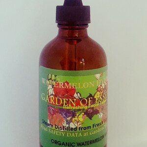 May include: A brown glass bottle with a black dropper top. The label reads "WATERMELON HYDRATE GARDEN OF ESSENCE Refreshing Facial Toner". The label is green with floral illustrations and text. The bottle contains a clear liquid.