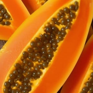 K&ouml;nnte beinhalten: Mehrere H&auml;lften einer reifen Papaya mit leuchtend orangefarbenem Fruchtfleisch und einer zentralen H&ouml;hle, die mit zahlreichen kleinen, runden, dunkelbraunen bis schwarzen Samen gef&uuml;llt ist. Die Textur des Fruchtfleisches wirkt glatt und feucht.