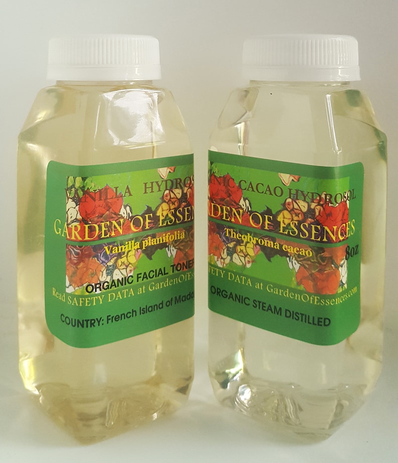 May include: Two clear glass bottles with white lids, filled with a light yellow liquid. The bottles are labeled "Garden of Essences" with the names of the essential oils, "Vanilla planifolia" and "Theobroma cacao", and the size, "8 oz". The labels also include the text "Organic Facial Tone", "Organic Steam Distilled", and "Read Safety Data at GardenOfEssences.com".