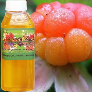 Puede incluir: Una botella transparente con tapa blanca y etiqueta verde. La etiqueta dice "LOUDBERRY SEED GARDEN OF ESSENCE" y "ORGANIC COLD PRESSED UNREFINED." Junto a la botella, varias bayas de los pantanos de color naranja.