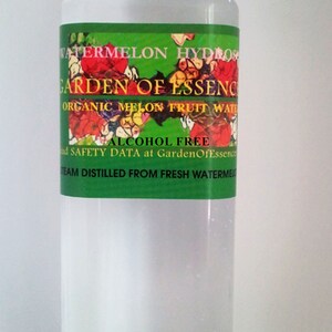 May include: A clear plastic bottle with a white cap, filled with a transparent liquid. The label features the text "Watermelon Hydrosol" and "Garden of Essence" with floral illustrations. The label also states "Alcohol Free".