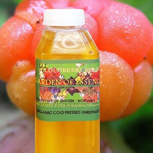 Puede incluir: Una botella transparente con tapa blanca llena de l&iacute;quido amarillo. La etiqueta dice "Cloudberry Seed Garden of Essence" y "Organic Cold Pressed Unrefined". El fondo presenta bayas de los pantanos de color naranja.