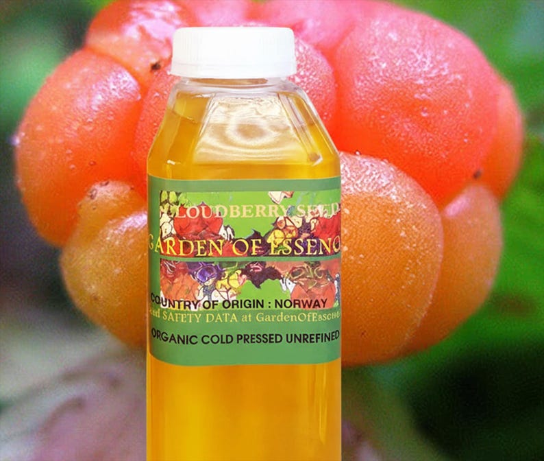 Puede incluir: Una botella transparente con tapa blanca llena de l&iacute;quido amarillo. La etiqueta dice "Cloudberry Seed Garden of Essence" y "Organic Cold Pressed Unrefined". El fondo presenta bayas de los pantanos de color naranja.