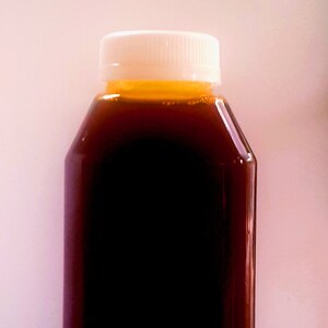 May include: A clear glass bottle with a white lid filled with a dark brown liquid. The liquid has a slight orange hue at the top.