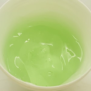 May include: A white bowl filled with a light green gel. The gel has a smooth, translucent texture.