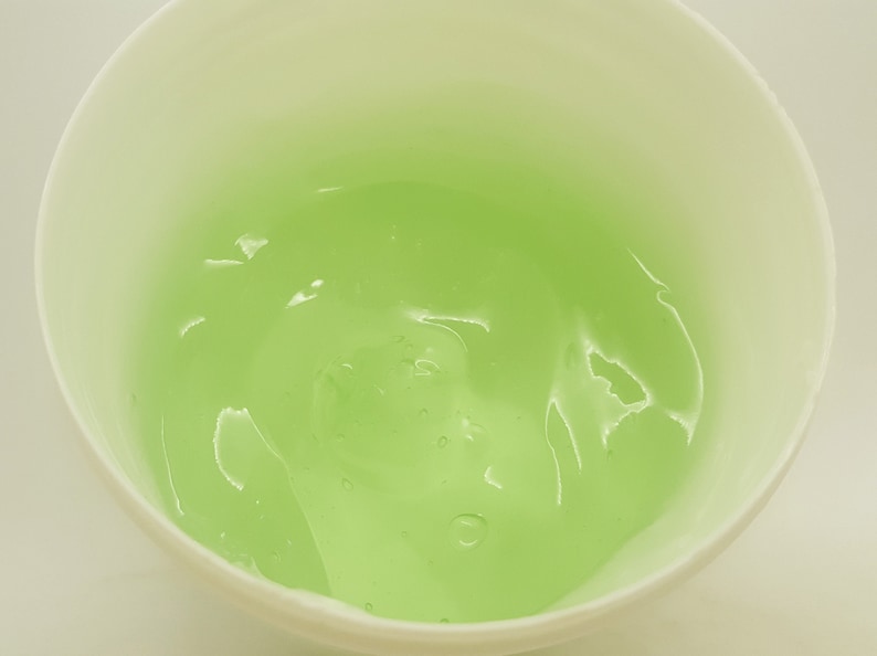 May include: A white bowl filled with a light green gel. The gel has a smooth, translucent texture.