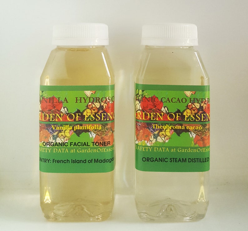 May include: Two clear glass bottles with green and white labels. The labels say "Garden of Essen" and list the ingredients as "Vanilla planifolia" and "Theobroma cacao". One bottle is labeled "Organic Facial Toner" and the other is labeled "Organic Steam Distilled".
