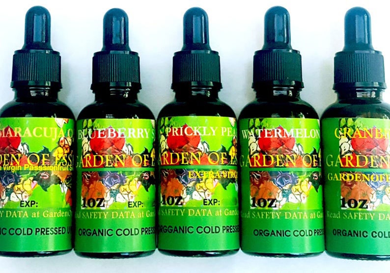 Puede incluir: Cinco botellas de vidrio oscuro con cuentagotas negros, cada una etiquetada con una fruta diferente: Maracujao, Ar&aacute;ndano, Tuna, Sand&iacute;a y Ar&aacute;ndano rojo. Las etiquetas son verdes con ilustraciones de frutas y texto, incluyendo "Garden of..."