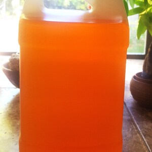 May include: A large, rectangular, translucent plastic jug filled with a vibrant orange liquid. The container features a sturdy integrated handle at the top and is sealed with a simple, circular, light gray screw-on cap at the top right corner.