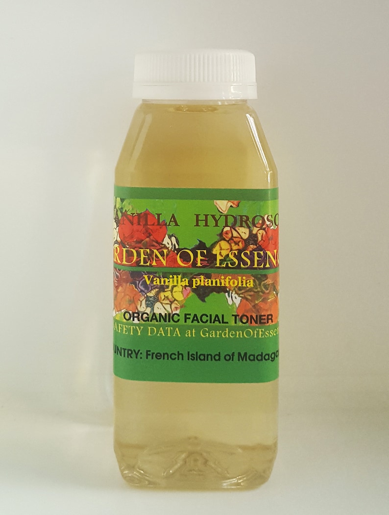 May include: A clear glass bottle with a white cap filled with a light yellow liquid. The label reads "Vanilla planifolia Organic Facial Toner" and "Safety Data at GardenOfEssen" and "Country: French Island of Madagascar".