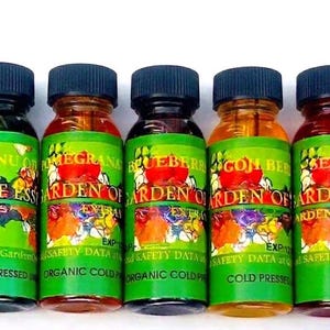 May include: A row of small glass bottles with black caps, each labeled with a different fruit or plant extract. The labels are green with colorful floral designs and text that reads "Garden of Eden".