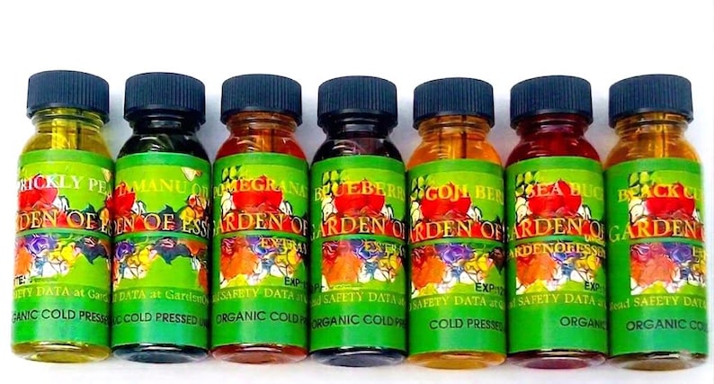 May include: A row of small glass bottles with black caps, each labeled with a different fruit or plant extract. The labels are green with colorful floral designs and text that reads "Garden of Eden".