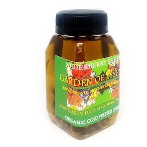 May include: A clear, square bottle with a black cap, filled with a golden liquid. A green label displays the text "ELDERBERRY SEED GARDEN OF ESSE" and "ORGANIC COLD PRESSED UNRE". The bottle is on a white background.