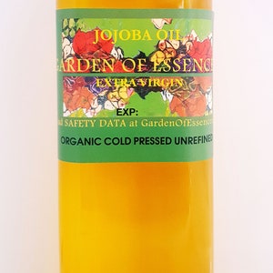May include: A clear glass bottle of organic, cold-pressed, extra virgin jojoba oil. The bottle has a white cap and a green label with the text "JOJOBA OIL GARDEN OF ESSENCE EXTRA VIRGIN EXP: ad SAFETY DATA at GardenOfEssences ORGANIC COLD PRESSED UNREFINED".