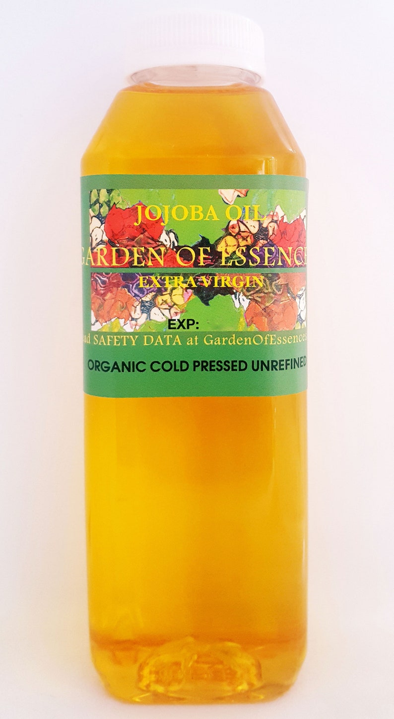 May include: A clear glass bottle of organic, cold-pressed, extra virgin jojoba oil. The bottle has a white cap and a green label with the text "JOJOBA OIL GARDEN OF ESSENCE EXTRA VIRGIN EXP: ad SAFETY DATA at GardenOfEssences ORGANIC COLD PRESSED UNREFINED".