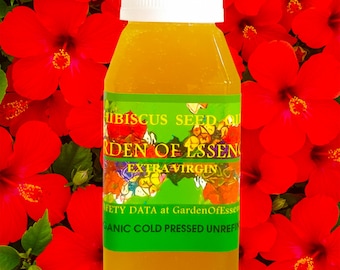 May include: A clear bottle with a white cap filled with yellow liquid, labeled "HIBISCUS SEED OIL GARDEN OF ESSENCE EXTRA VIRGIN." The background features vibrant red hibiscus flowers and green leaves.
