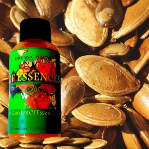 Puede incluir: Una botella de aceite de semilla de calabaza org&aacute;nico con una tapa negra y una etiqueta verde con el texto "Garden Of Essences". La botella est&aacute; rodeada de semillas de calabaza, con las palabras "Unrefined Cold Pressed" en la parte inferior.