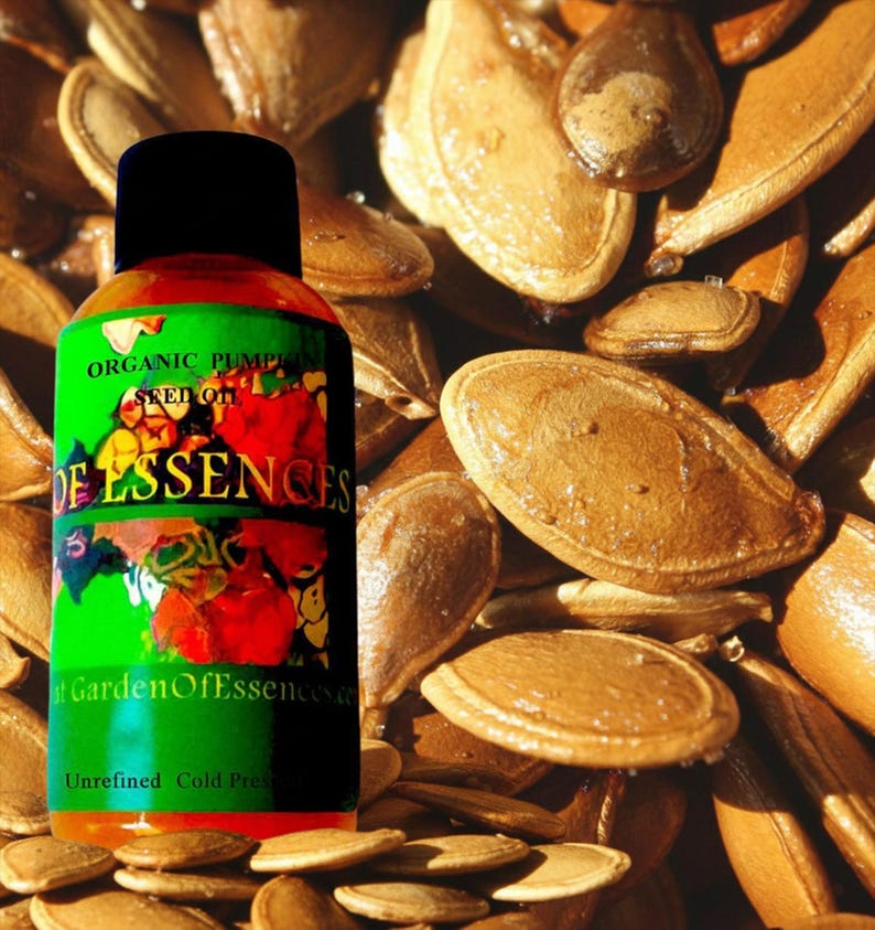 Puede incluir: Una botella de aceite de semilla de calabaza org&aacute;nico con una tapa negra y una etiqueta verde con el texto "Garden Of Essences". La botella est&aacute; rodeada de semillas de calabaza, con las palabras "Unrefined Cold Pressed" en la parte inferior.