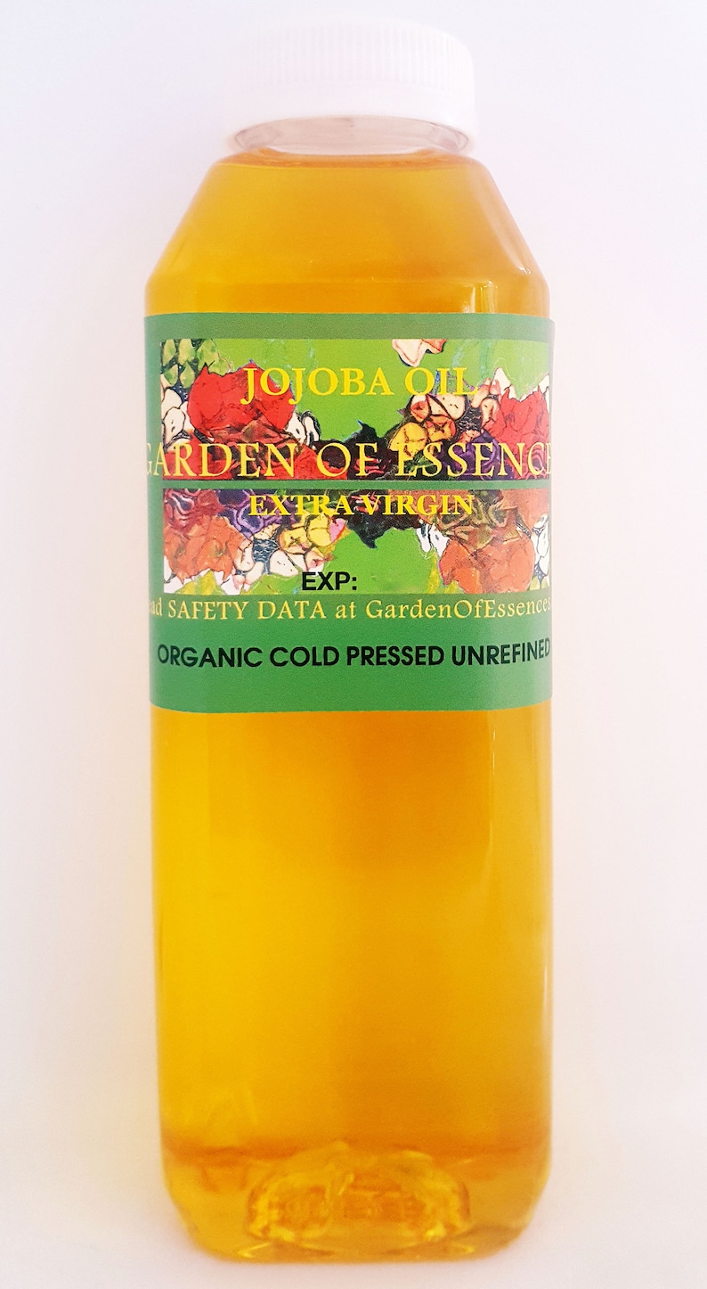 May include: A clear glass bottle of organic, cold-pressed, extra virgin jojoba oil. The bottle has a white cap and a green label that reads "Jojoba Oil Garden of Essence Extra Virgin" and "Organic Cold Pressed Unrefined".