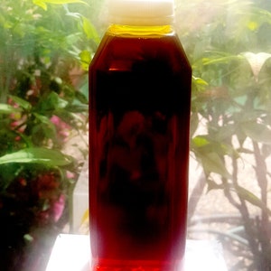 May include: A clear plastic bottle with a white lid filled with a dark red liquid. The bottle is sitting on a white surface.