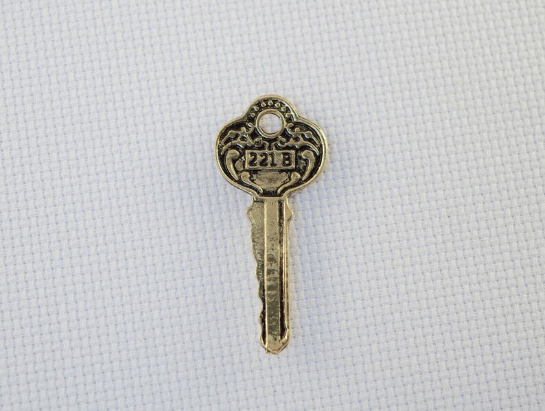 May include: A gold-coloured key with intricate details on the head. The key has a black number "221B" on the head.