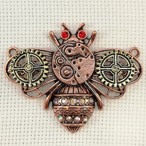 May include: A bronze-colored bee charm with intricate gear details and red rhinestone accents. The bee's body is adorned with clear rhinestones.