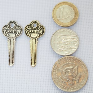 May include: Two gold-coloured keys with the number 221 B on them, next to three coins: a Euro coin, a Ten Pence coin, and a half dollar coin.