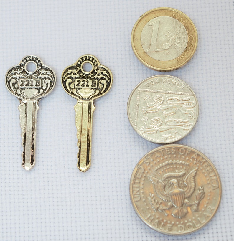 May include: Two gold-coloured keys with the number 221 B on them, next to three coins: a Euro coin, a Ten Pence coin, and a half dollar coin.
