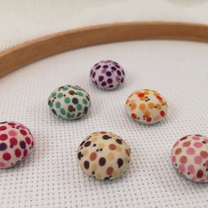 May include: Six colourful fabric pincushions with polka dot patterns. The pincushions are arranged in a circle on a white surface.