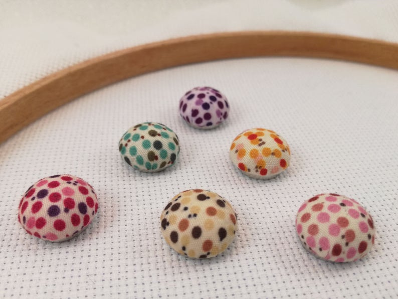 May include: Six colourful fabric pincushions with polka dot patterns. The pincushions are arranged in a circle on a white surface.