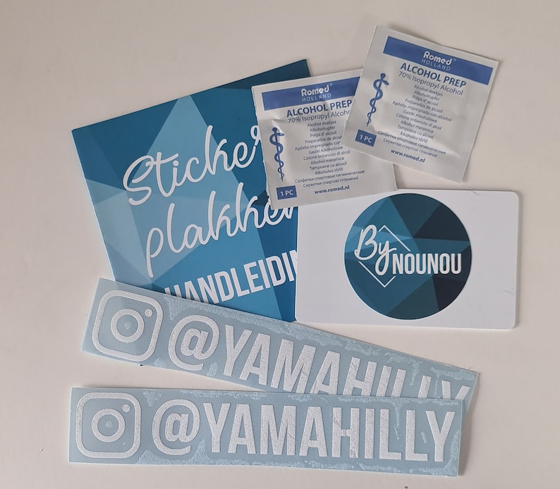 以下が含まれることがあります： 青と白のステッカーシートに、白で「Sticker Plakkers」と「Handleiding」の文字が書かれています。ステッカーシートの隣には、青い円と白で「By Nounou」の文字が書かれた白いカードがあります。白の小さな袋が2つあり、黒で「Romed Holland Alcohol Prep 70% Isopropyl Alcohol」の文字が書かれています。白のステッカーが2つあり、白で「@Yamahahily」の文字が書かれています。