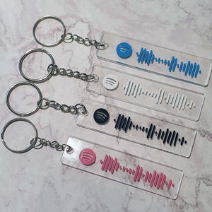 Op de afbeelding: Vier transparante acryl sleutelhangers met verschillende gekleurde Spotify-barcodes. Elke sleutelhanger heeft een zilveren metalen ring en een zilveren ketting.