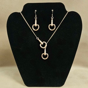 Puede incluir: Un conjunto de collar y pendientes de oro con un colgante de doble anillo en forma de bocado de caballo.