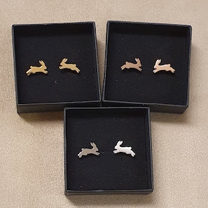 May include: Three small black boxes with gold, rose gold, and silver bunny rabbit earrings inside. The boxes are lined with black velvet.